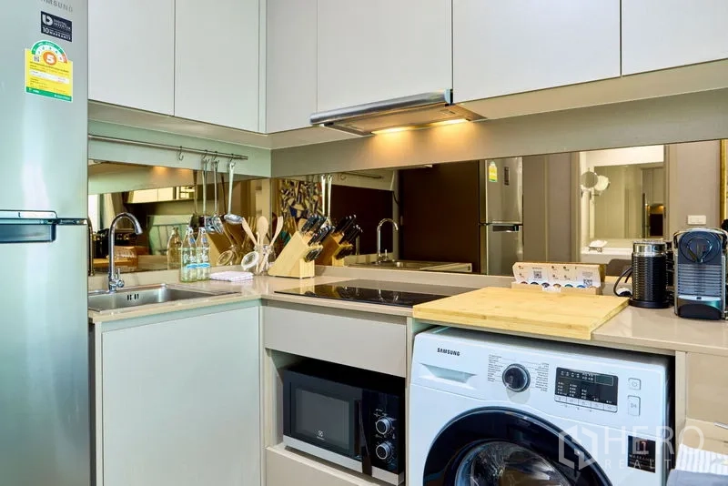 Condominium for rent in Phra Khanong, Bangkok - Close-up of L-shaped kitchen with induction hob, microwave, washer-dryer and coffee station.
