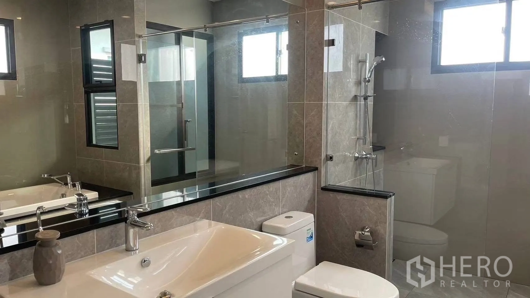 Detached House for rent in Prawet, Bangkok - Contemporary bathroom with large mirror, long vanity, toilet and glass-enclosed shower.