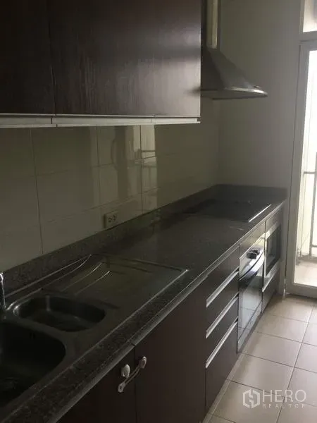 คอนโด ให้เช่าในWatthana, Bangkok - ครัวรูปตัวแกลลอรี่ ตู้ไม้สีเข้ม เคาน์เตอร์หิน เตาไฟฟ้า เตาอบ เครื่องดูดควัน และประตูสู่ระเบียงซักล้าง