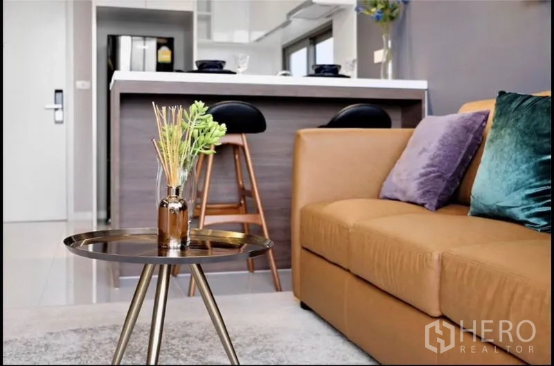 Condominium for rent in Bang Rak, Bangkok - Living area close-up showing tan leather sofa and round coffee table with kitchen island behind.