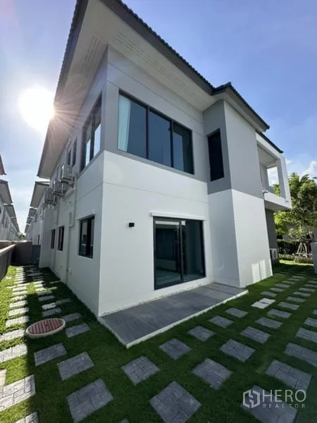 独立式住宅 出租在Bang Phli, Samut Prakan - 房屋后角，草坪、踏步石与大面积窗户。