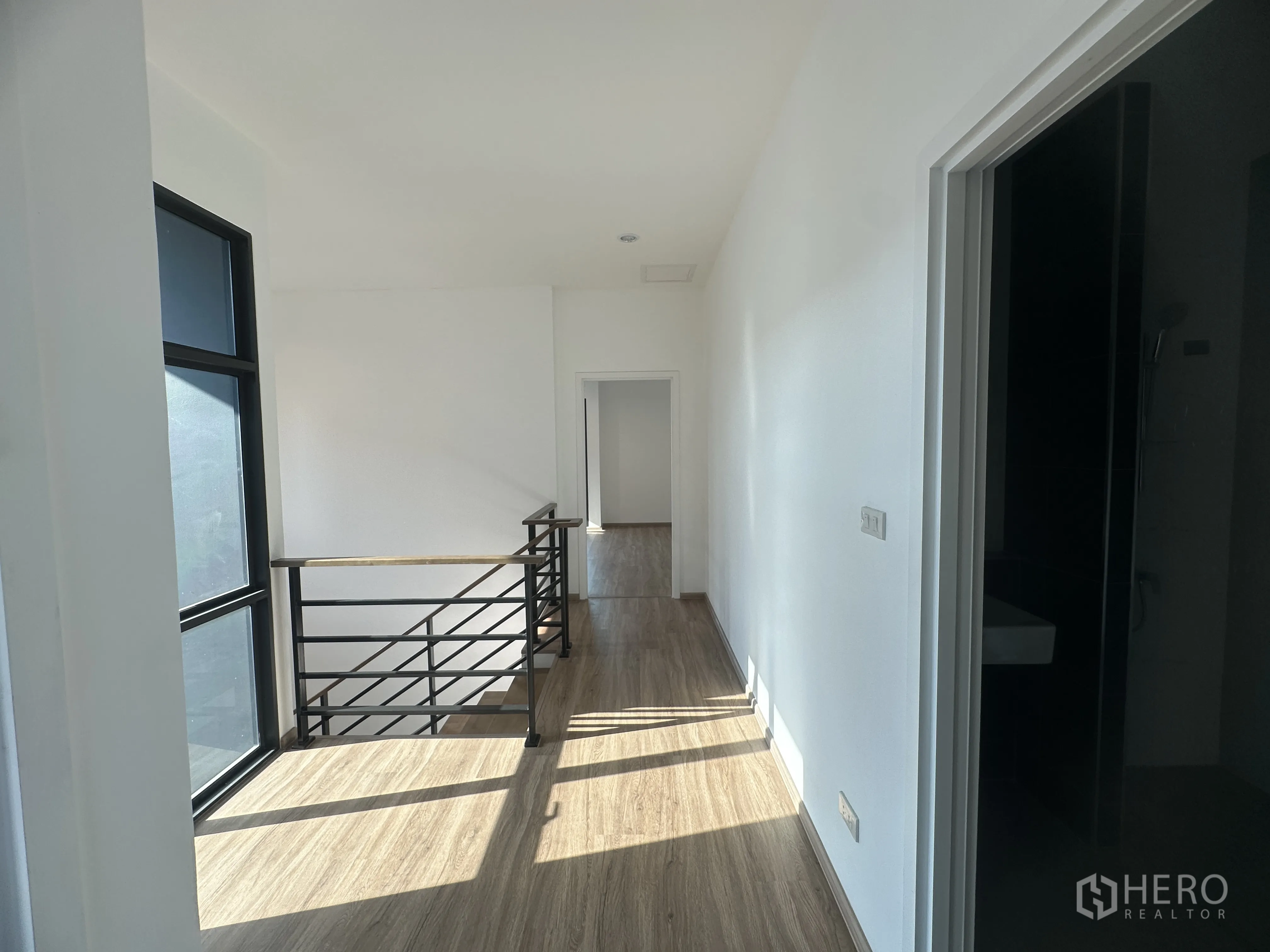Home Office for sale in Khlong Luang, Pathum Thani - Sunlit landing with large window, wood floors, and black metal stair railing.