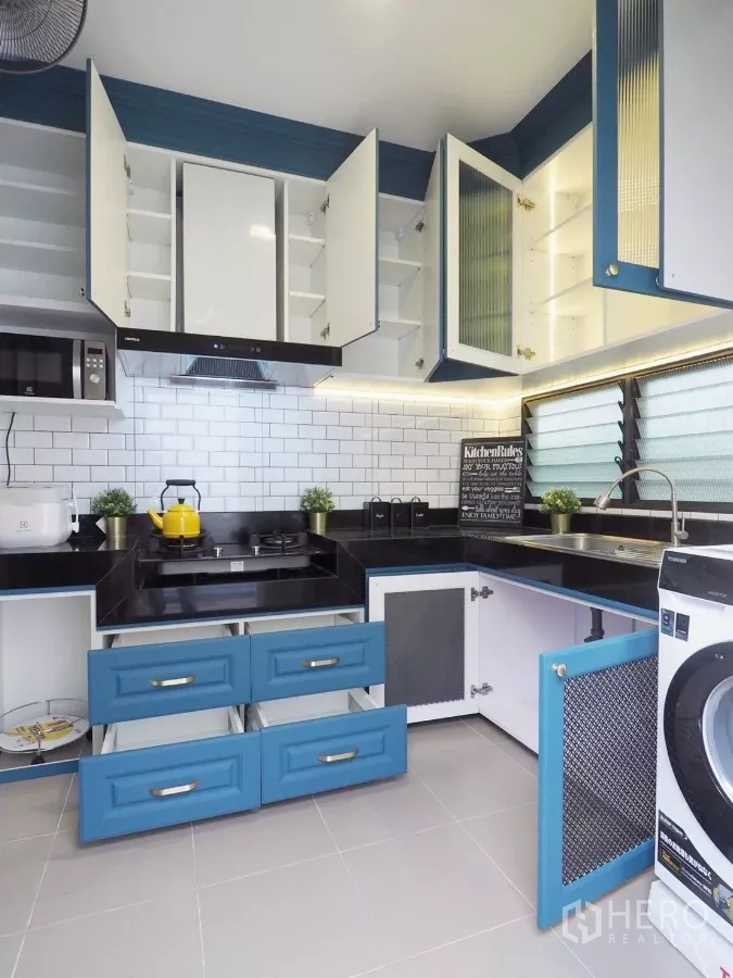 Detached House for sale in Bang Phli, Samut Prakan - Separate Thai kitchen with white subway tiles, blue cabinets, gas hob, sink and open storage.