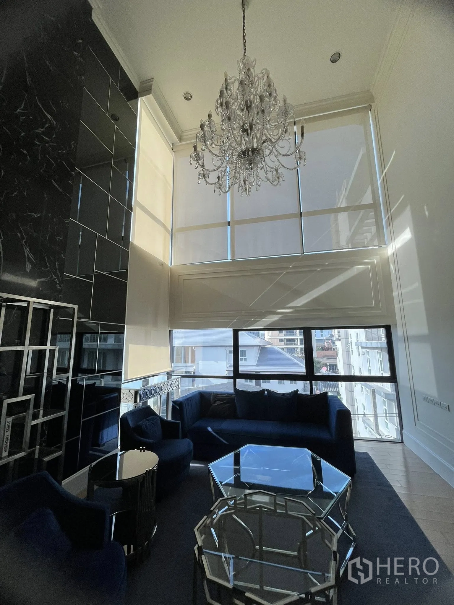 Home Office for rent in Watthana, Bangkok - Double-height living lounge with chandelier, tall windows, and blue sofas.