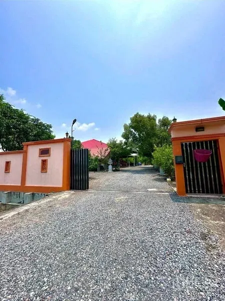 Detached House for sale in Bang Bua Thong, Nonthaburi - Front gate and wide driveway framed by trees on a sunny day.