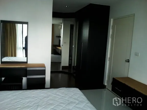 Condominium for rent in Watthana, Bangkok - Primary bedroom with dressing table, mirror, and built-in wardrobe in dark wood tones.