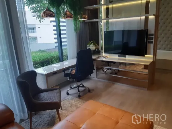 Condominium for rent or sale in Watthana, Bangkok - Built-in TV wall with LED lighting and a long window-side desk overlooking greenery.