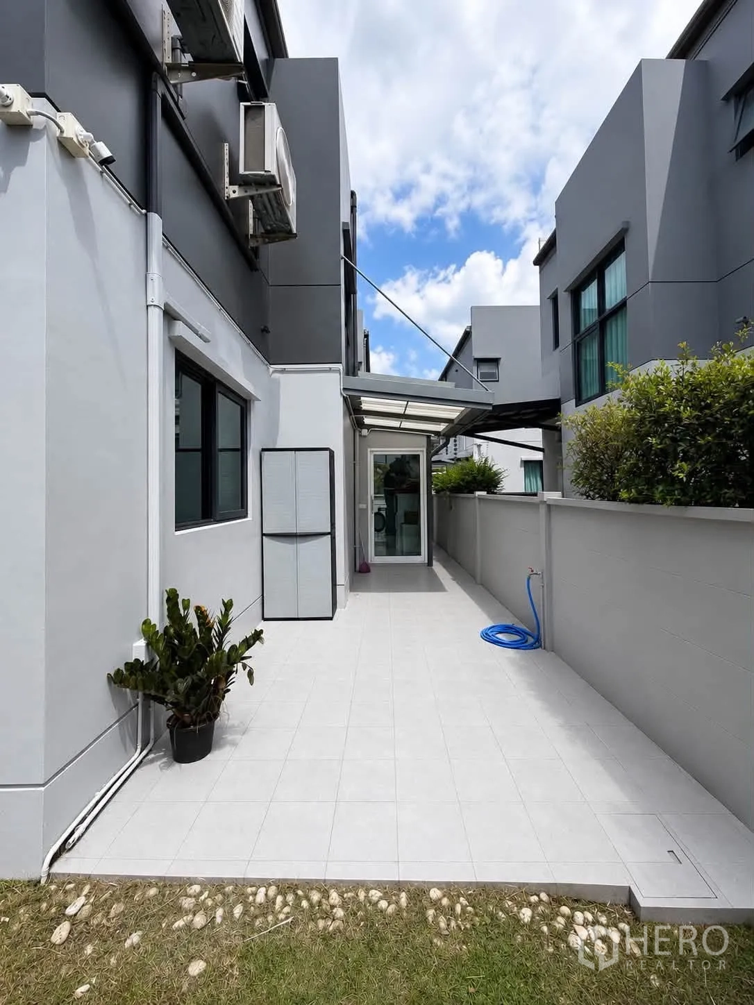 บ้านเดี่ยว for rent in Bang Phli, Samut Prakan - ลานกระเบื้องด้านข้างมีกันสาด เครื่องปรับอากาศภายนอก และสายยางรดน้ำ.