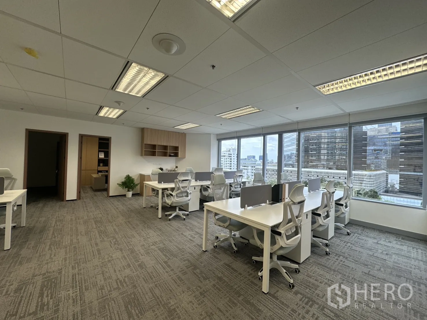 办公室 for rent in Pathum Wan, Bangkok - 临窗工位，窗外可见城市建筑与树木景观。
