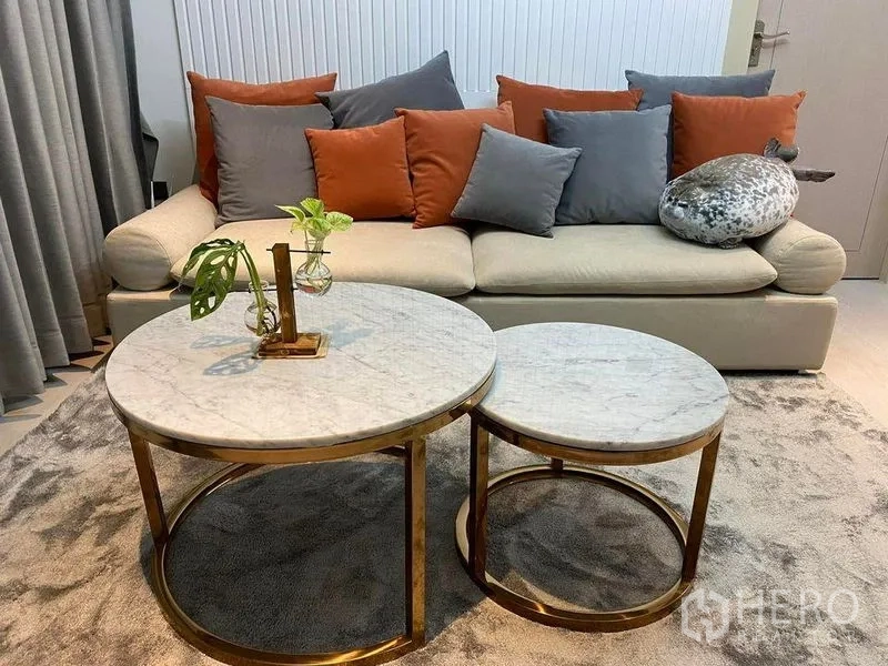 公寓 出售在Huai Khwang, Bangkok - 客厅一隅，米色沙发、橙灰抱枕，金框圆形大理石套叠茶几。