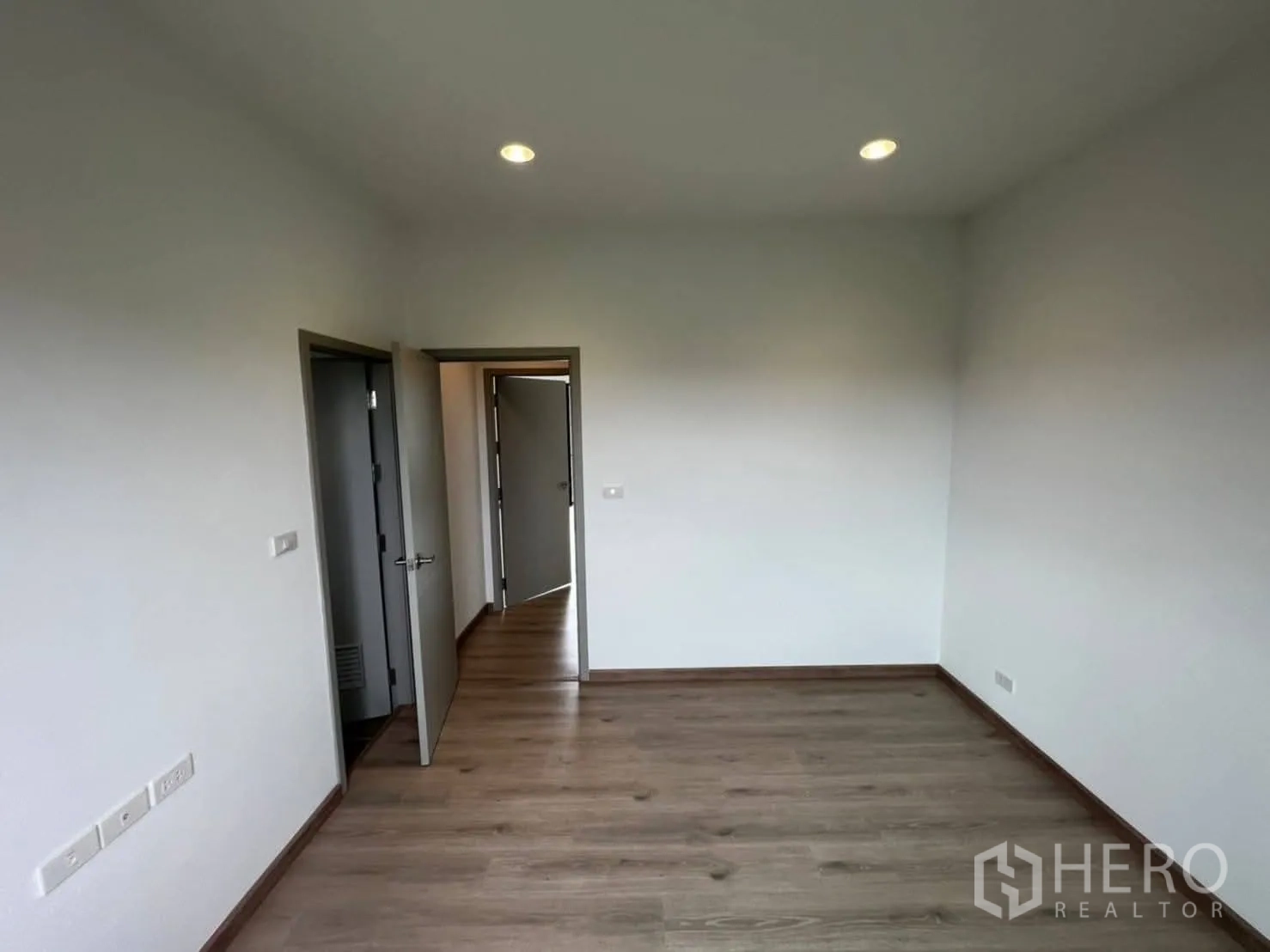 Townhouse for rent in Bang Khen, Bangkok - Bright bedroom with wood floors, white walls, and doorway to the hall.