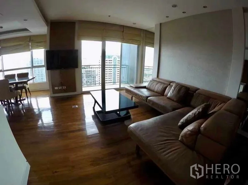 Condominium for rent or sale in Khlong San, Bangkok - Living room with leather sectional sofa, coffee table and balcony overlooking the city.
