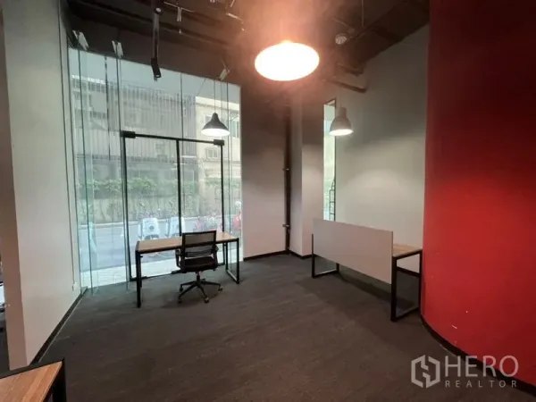 办公空间 出租 - 角落工位，落地玻璃临街视野，书桌转椅与红色弧形墙。