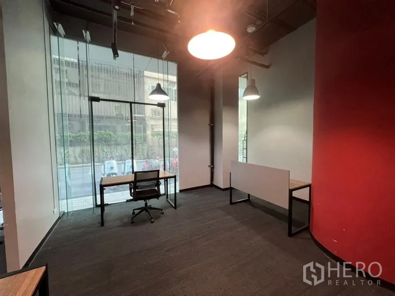 办公空间 出租 - 角落工位，落地玻璃临街视野，书桌转椅与红色弧形墙。