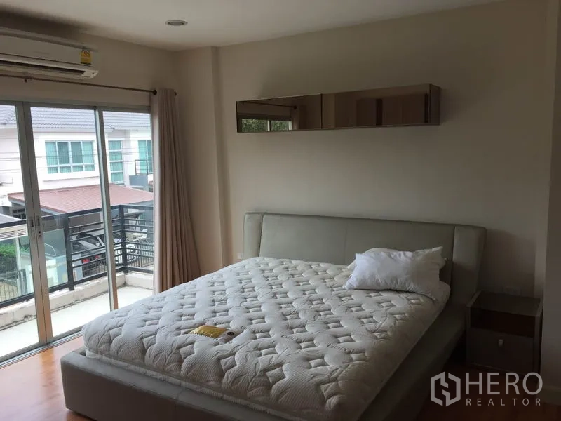 Detached House for rent or sale in Saphan Sung, Bangkok - Master bedroom with large bed, sliding glass doors to a balcony and wall-mounted air-conditioner.