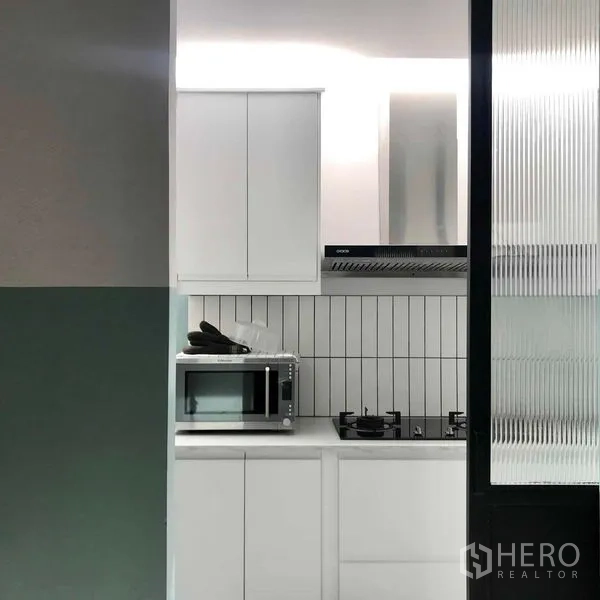 Townhouse for rent or sale in Khlong Toei, Bangkok - Compact white pantry kitchen with stove, microwave and fluted glass door.