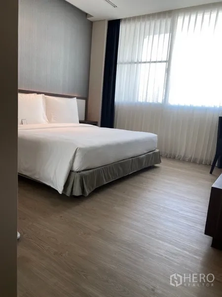 Apartment for rent in Khlong Toei, Bangkok - Spacious bedroom with king bed, wood floors and large curtained window providing natural light.