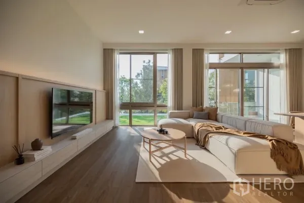 Detached House for rent in Saphan Sung, Bangkok - Sunlit living room with L-shaped sofa, TV wall and floor-to-ceiling windows overlooking the lawn.