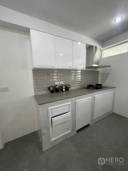 Townhouse for rent in Khlong Toei, Bangkok - Modern white kitchenette with glossy cabinets, subway tile backsplash and cooktop.