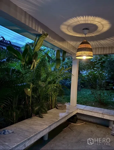 独立式住宅 出租在Watthana, Bangkok - 花园环绕的有顶露台，编织吊灯与大理石长凳座位。