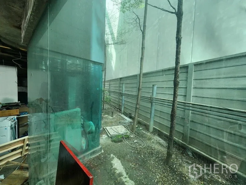 Retail Space for rent - Glass corner and narrow service yard with trees and utility lines along the boundary wall.