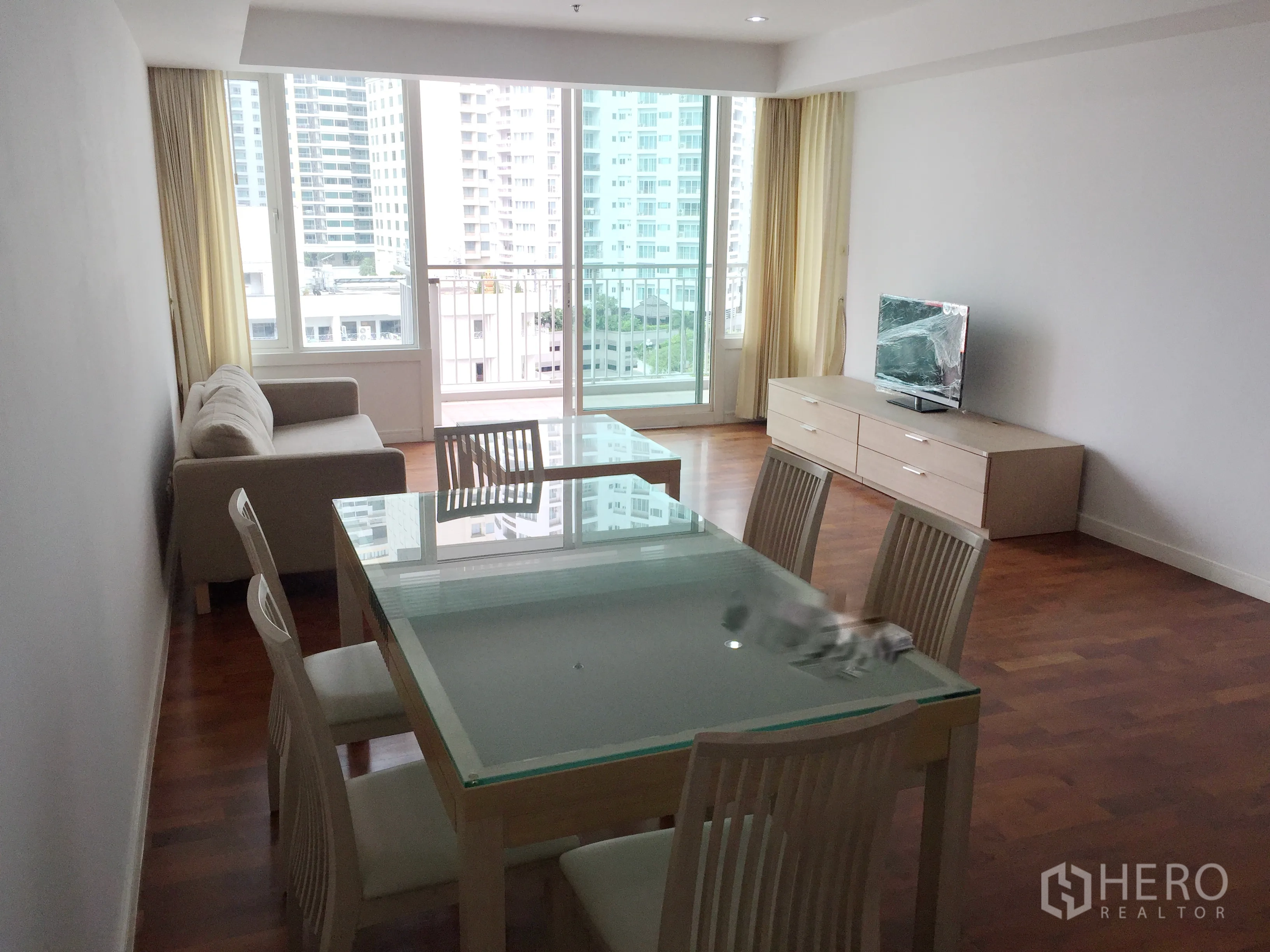 公寓 出租在Khlong Toei, Bangkok - 客餐厅一体，玻璃餐桌、沙发、电视与带城市景观的阳台。