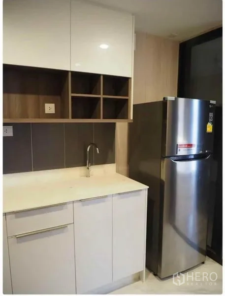 Condominium for rent in Huai Khwang, Bangkok - Modern kitchenette with quartz countertop, open shelves and stainless-steel refrigerator.