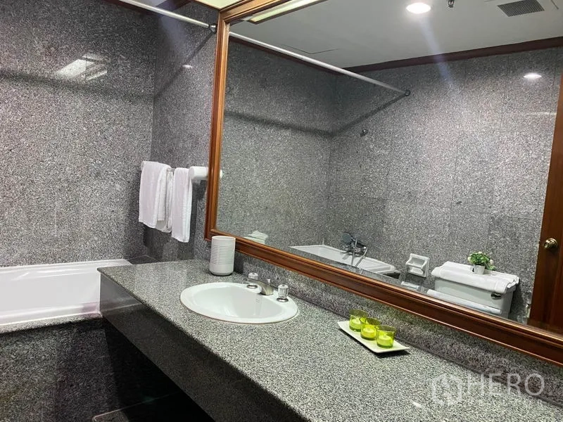 Condominium for rent in Watthana, Bangkok - Granite-tiled bathroom with wide vanity, large framed mirror, bathtub and toilet.