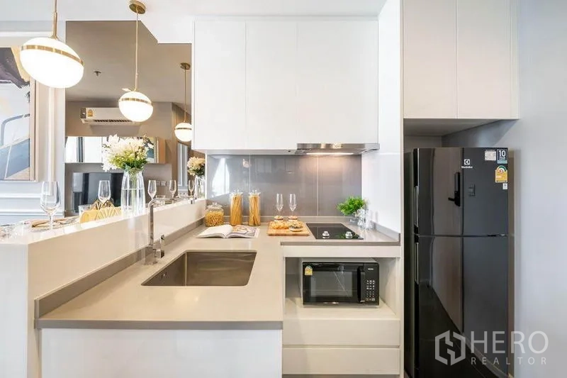 公寓 出租或出售在Watthana, Bangkok - 现代白色厨房，带吧台、水槽、电磁炉、微波炉和黑色冰箱。