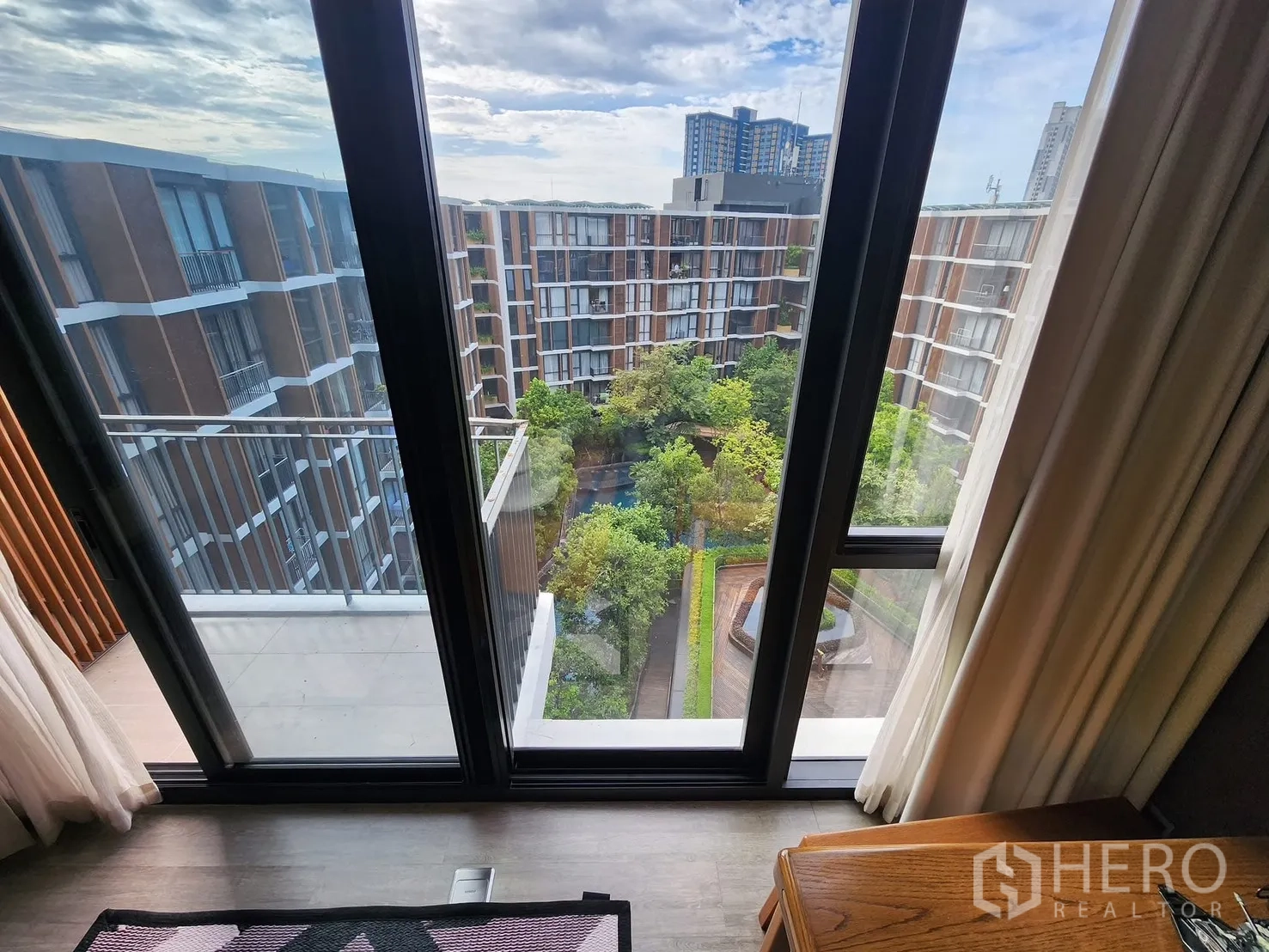 Condominium for rent in Watthana, Bangkok - Sliding glass doors opening to a balcony with views of the landscaped courtyard and neighboring buildings.