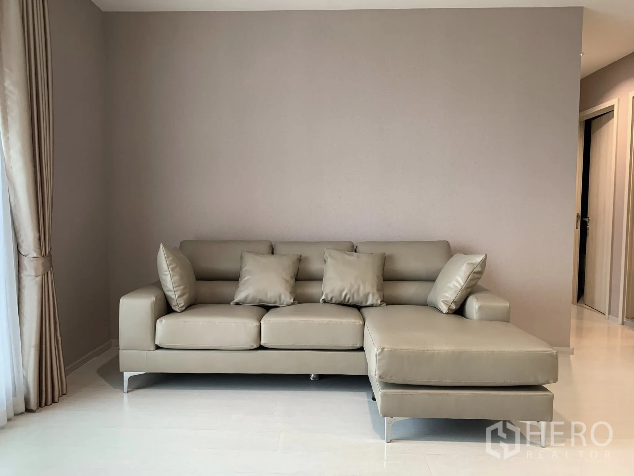 Condominium for rent in Khlong Toei, Bangkok - Living room with taupe L-shaped sofa, neutral walls, and floor-to-ceiling curtains.