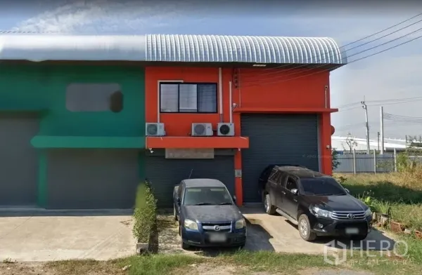 货栈 出售在Samut Prakan - 橙色仓库外立面，双卷闸门、弧形金属屋顶与停车位。