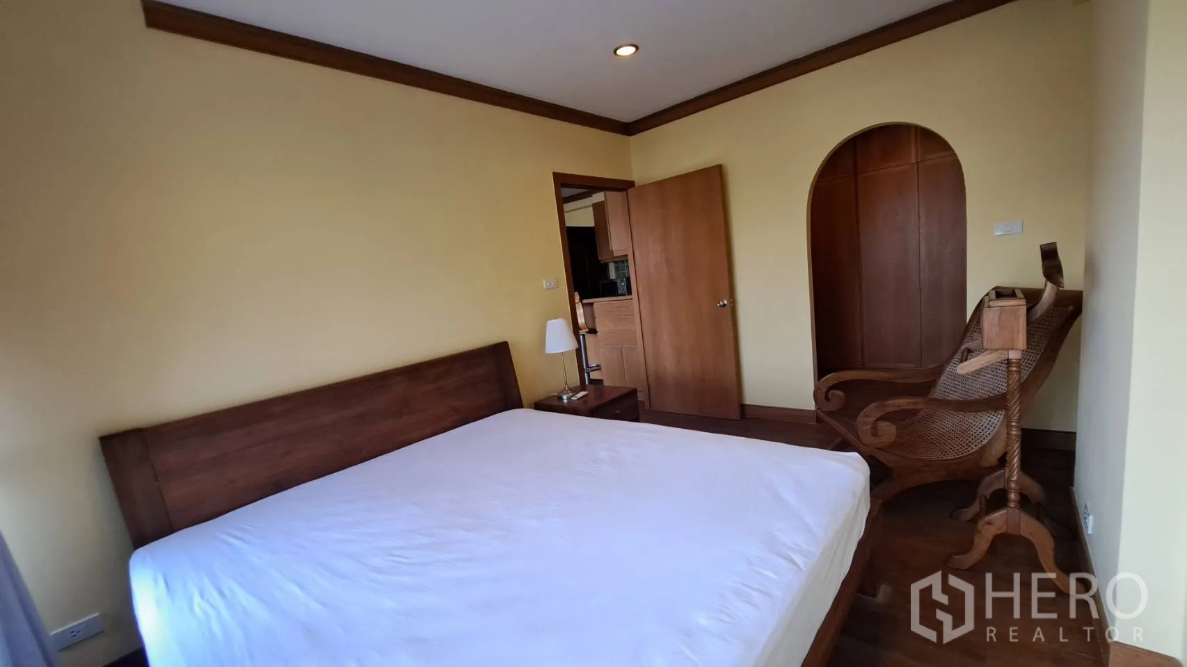 Condominium for rent in Khlong Toei, Bangkok - Bedroom with wooden bed, bedside lamp, and arched wardrobe niche.