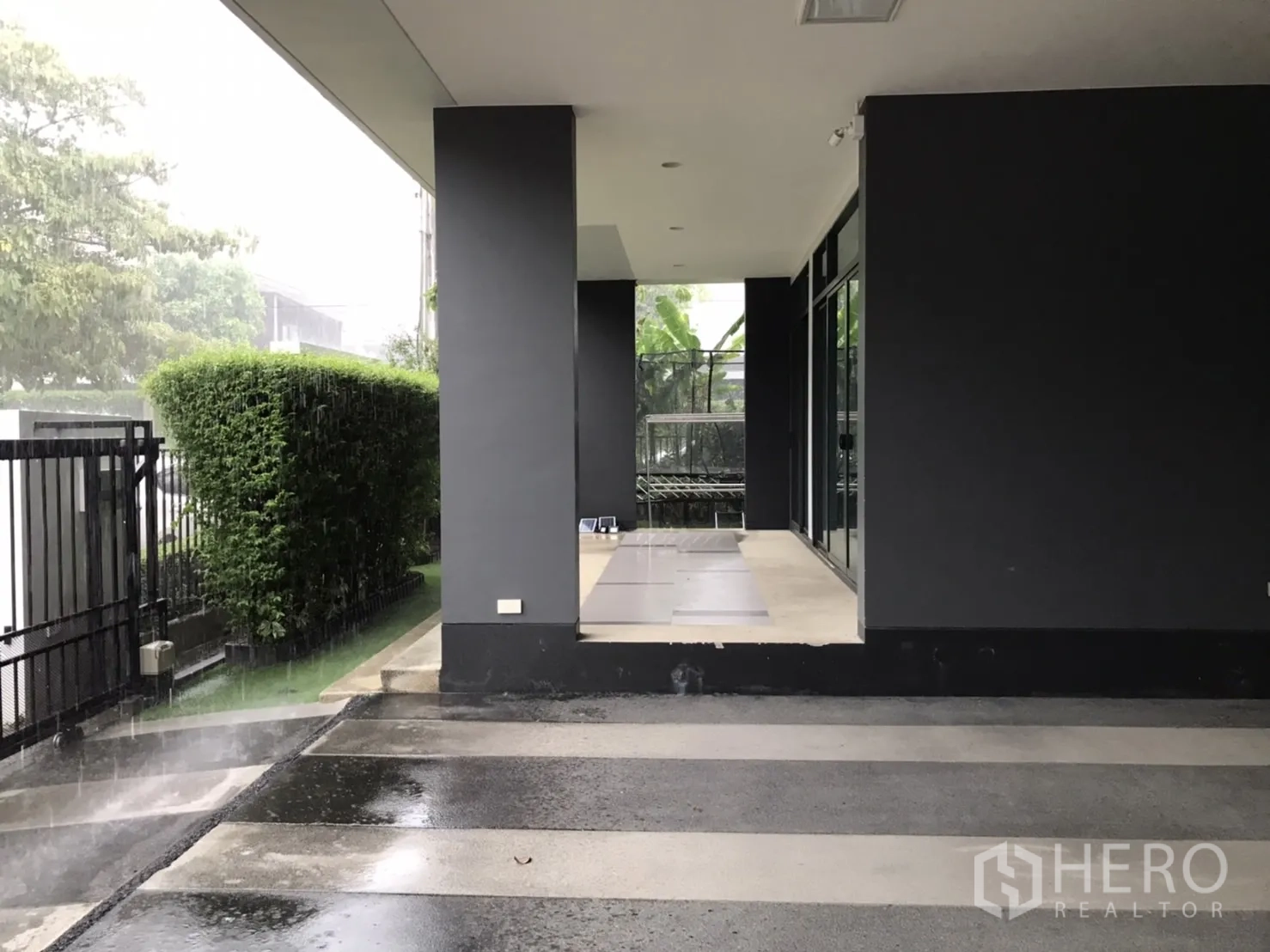 Detached House for rent in Bang Kapi, Bangkok - Covered terrace and carport beside a trimmed hedge and sliding glass doors.