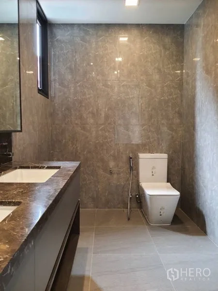 Condominium for sale in Huai Khwang, Bangkok - Spacious bathroom with double vanity, toilet and gray tiled walls.