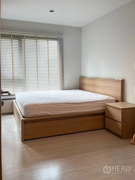 Condominium for sale in Ratchathewi, Bangkok - Bright bedroom with wooden bed frame, bedside table, and large window blinds.