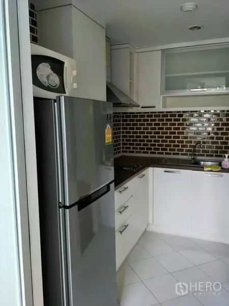 公寓 出租在Khlong Toei, Bangkok - L形厨房，白色橱柜，棕色地铁砖挡板，不锈钢冰箱、灶台与水槽