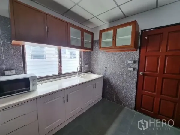 独立式住宅 出租在Nonthaburi - 配备白色台面与吊柜的厨房，设水槽和微波炉。