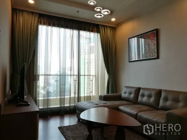 Condominium for rent in Sathon, Bangkok - Living room with L-shaped leather sofa, TV console and floor-to-ceiling glass doors opening to a balcony.