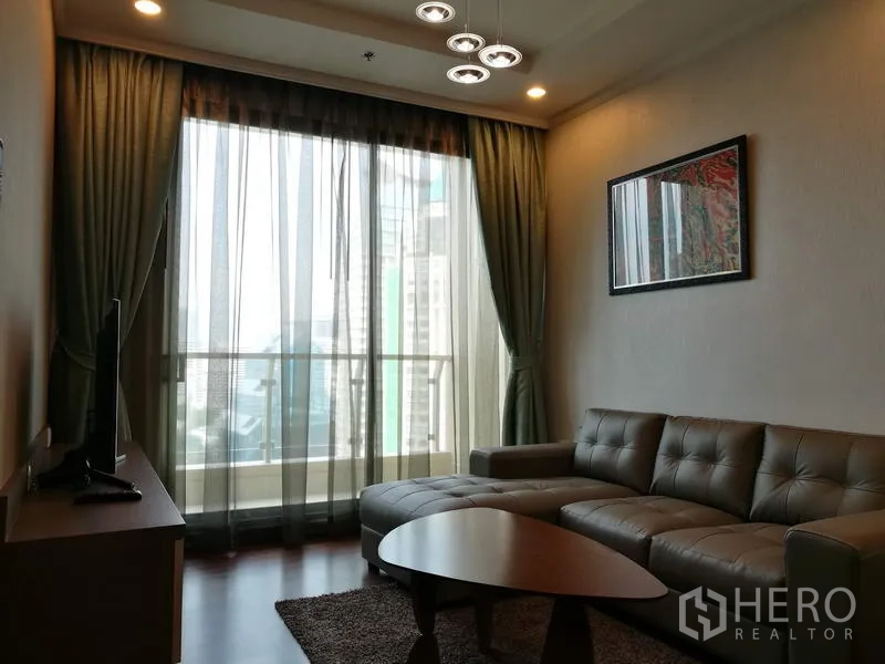 Condominium for rent in Sathon, Bangkok - Living room with L-shaped leather sofa, TV console and floor-to-ceiling glass doors opening to a balcony.
