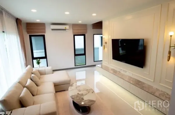 Detached House for rent in Bang Phli, Samut Prakan - Stylish living room with L-shaped sofa, wall-mounted TV and marble-top console.