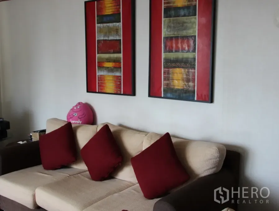 คอนโด ให้เช่าในKhlong Toei, Bangkok - ห้องนั่งเล่นอบอุ่น โซฟาสีครีม หมอนสีแดง และภาพศิลปะแบบนามธรรมสองชิ้นบนผนัง