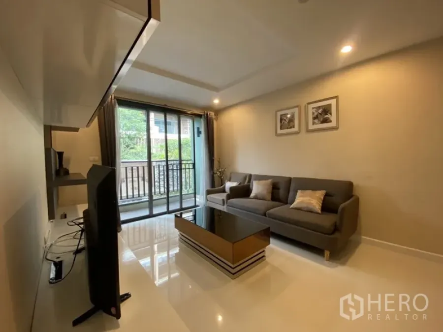 Condominium for rent in Watthana, Bangkok - Bright living room with gray sofa, TV console and sliding doors opening to a balcony with greenery view.