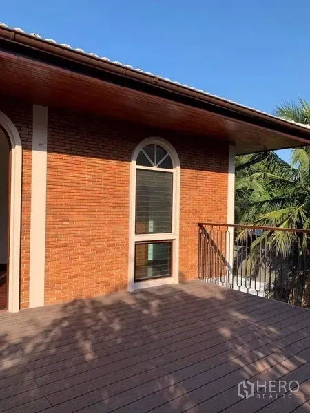 Detached House for rent in Ratchathewi, Bangkok - Upper balcony with wood decking, metal railing and an arched window on a brick facade.