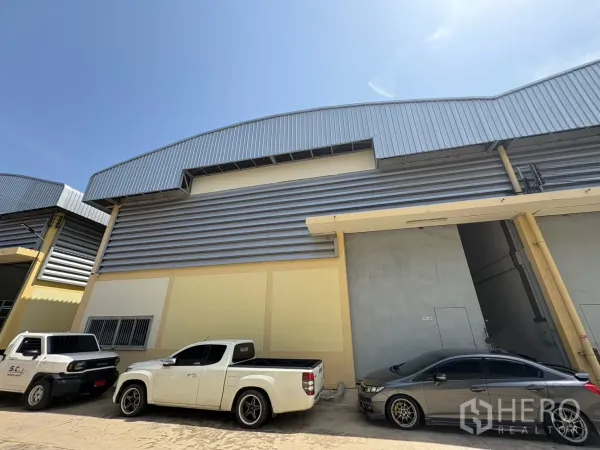 货栈 出租在Ban Phaeo, Samut Sakhon - 仓库外立面采用金属板与高挑屋顶，设大型装卸门，前方可停车。