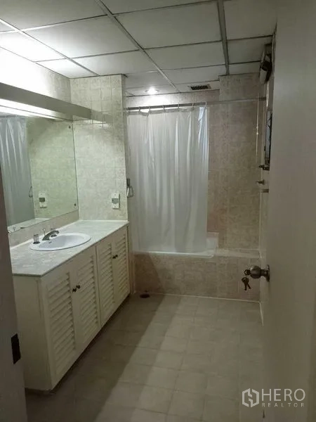 Condominium for rent in Watthana, Bangkok - Bathroom with long vanity, large mirror and bathtub with shower curtain.