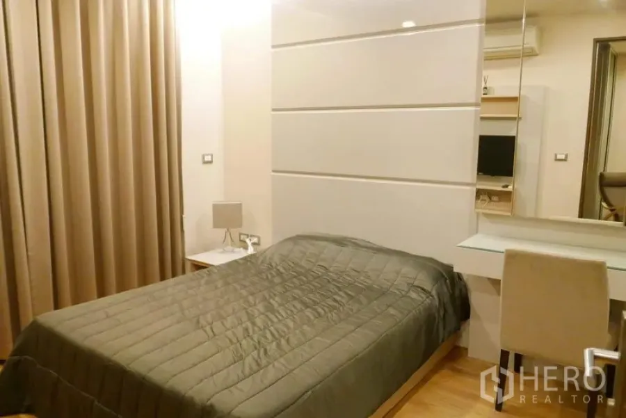 Condominium for rent in Ratchathewi, Bangkok - Warm bedroom with a double bed, padded headboard panels, full curtains and a built-in desk.