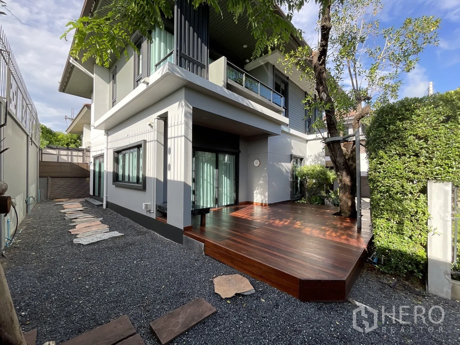 บ้าน ให้เช่าหรือขายในLam Luk Ka, Pathum Thani - ด้านข้างตัวบ้านพร้อมชานไม้ขนาดใหญ่ ประตูกระจกบานเลื่อน และทางเดินสวนโรยกรวด