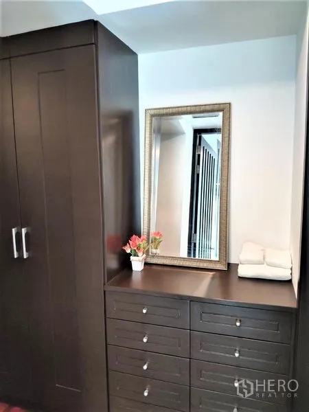 Condominium for rent in Bang Rak, Bangkok - Built-in dark wood wardrobe and dresser with a framed mirror and decor.