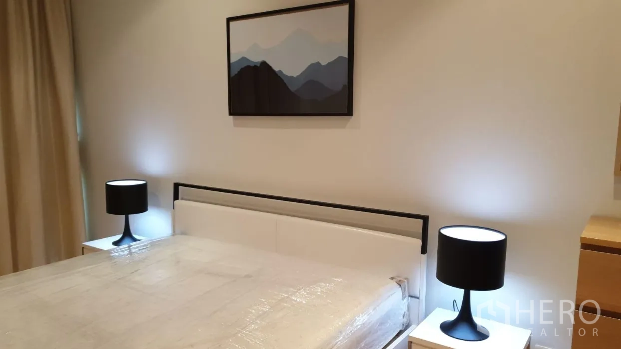 Condominium for rent or sale in Khlong Toei, Bangkok - Minimalist bedroom featuring a queen bed, twin bedside lamps, and framed wall art.